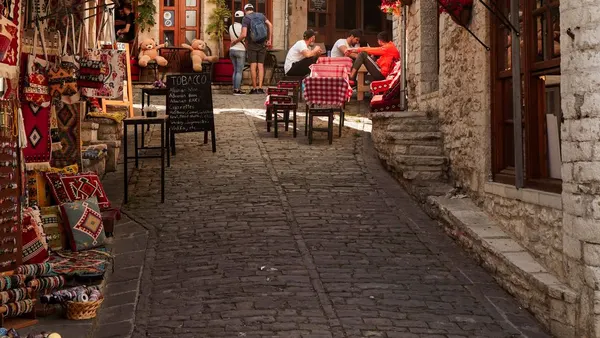 Brukowana uliczka Starego Bazaru w Gjirokastrze z rękodziełem i stolikami kawiarni